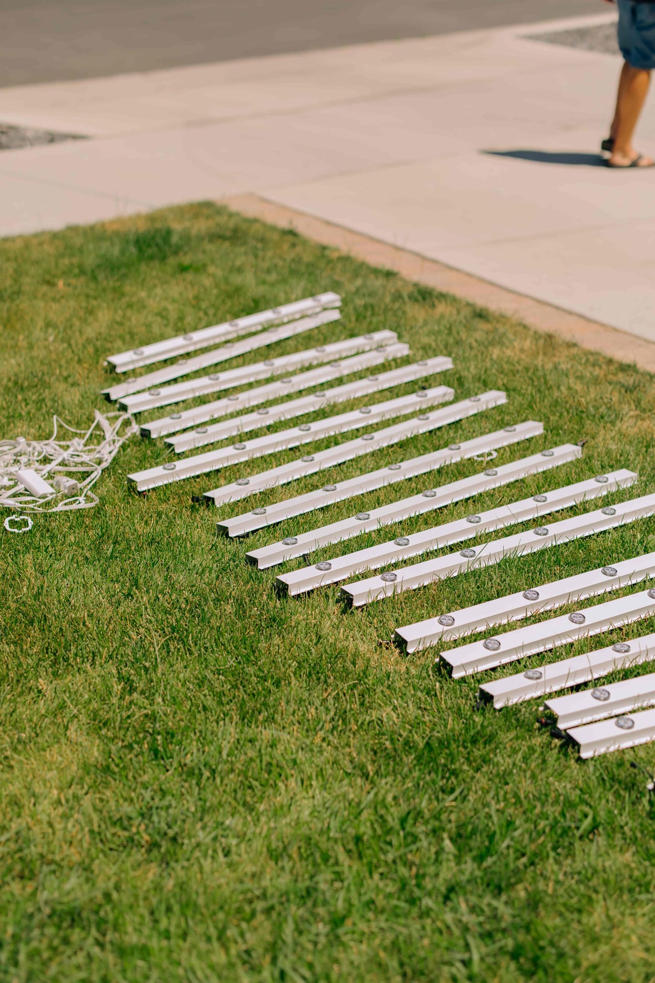 Permanent lighting track sections with individual LED nodes laid out on a lawn before installation