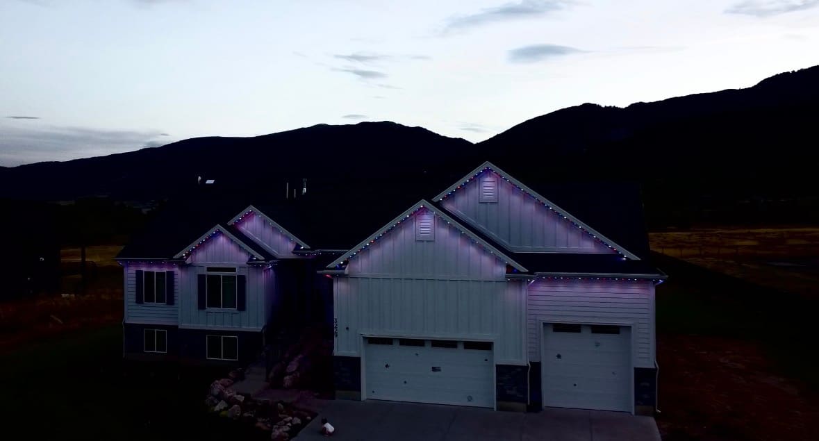 White board-and-batten craftsman with red, white, and blue gable lighting against a mountain backdrop