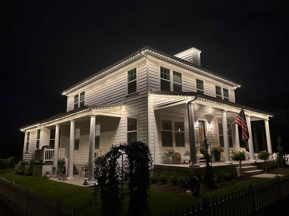 White two-story farmhouse with warm-white permanent lighting along the roofline