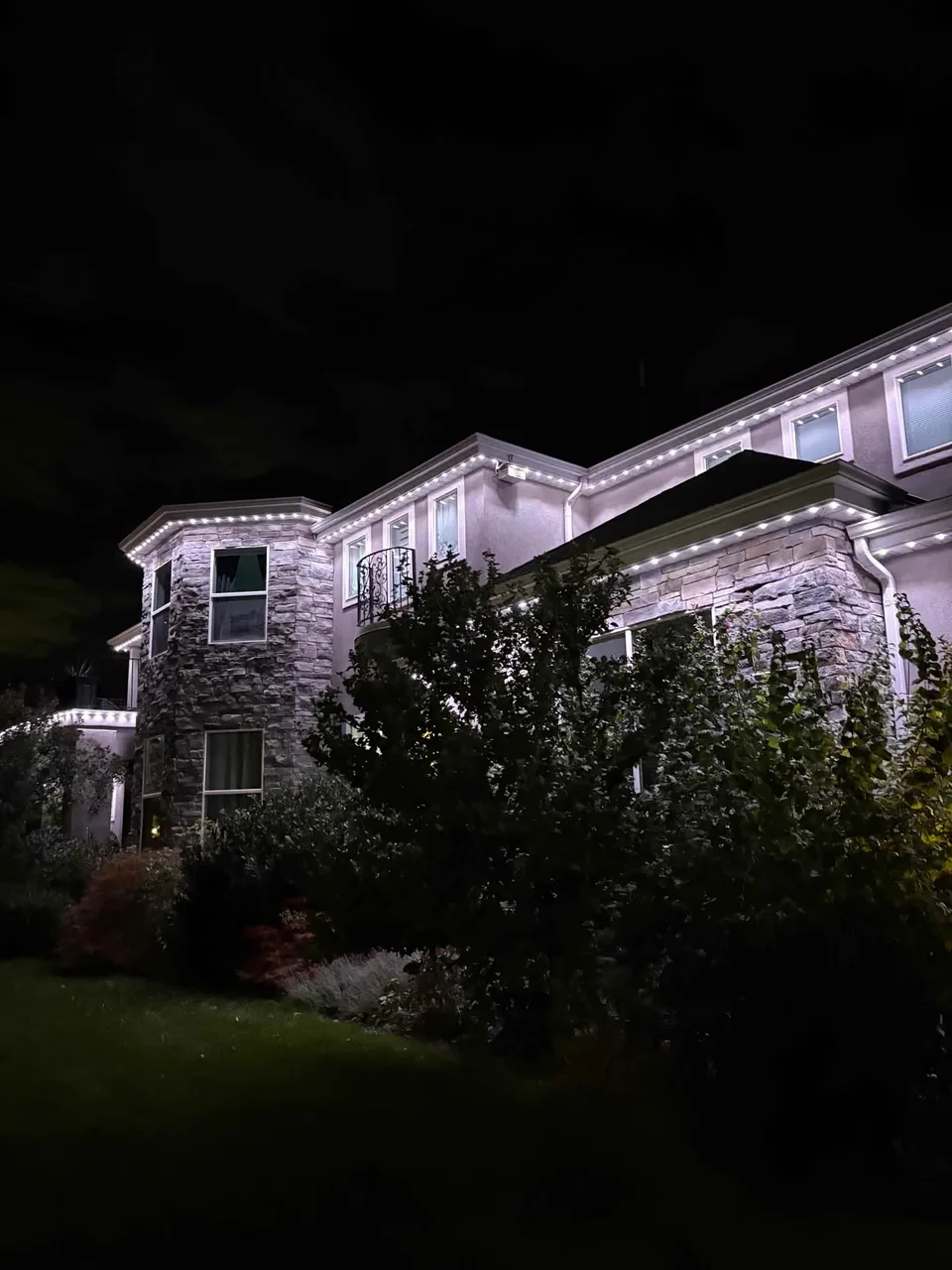 Two-story stone home with light-colored permanent roofline lighting