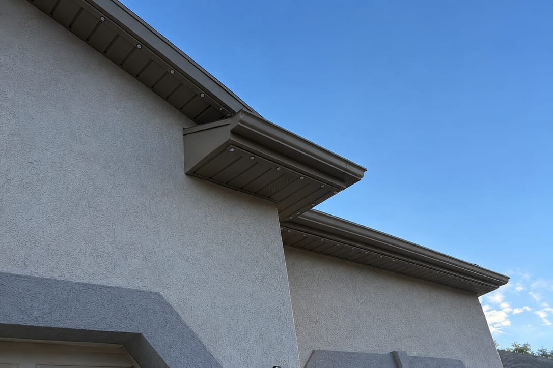 Brown and tan aluminum soffit and fascia with recessed lighting, color-matched to the home's stucco exterior