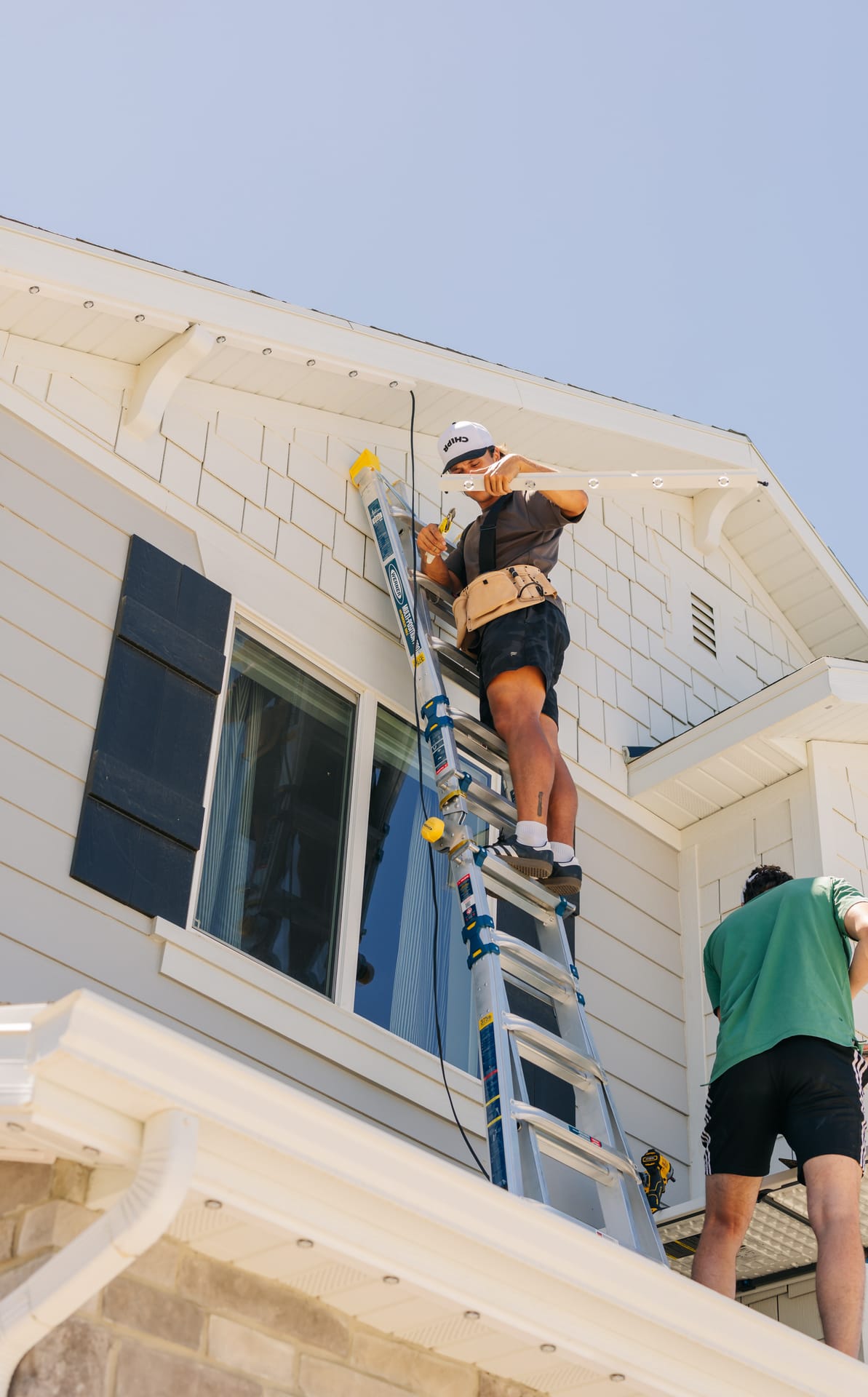 Chipr Lux installer on a ladder mounting permanent lighting track along a home's gable eave